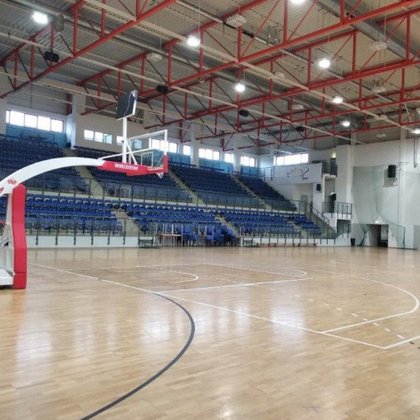 Wnętrze hali sportowej z boiskiem do koszykówki. W tle trybuny dla kibiców.